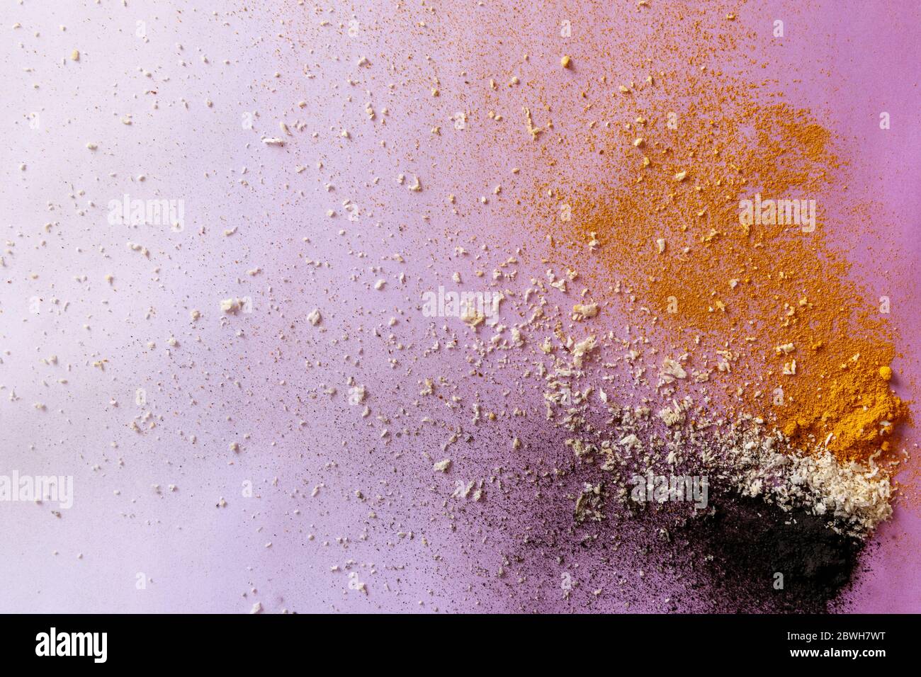 Violet background with colorful explosion of ingredients - activated carbon, coconut and turmeric Stock Photo