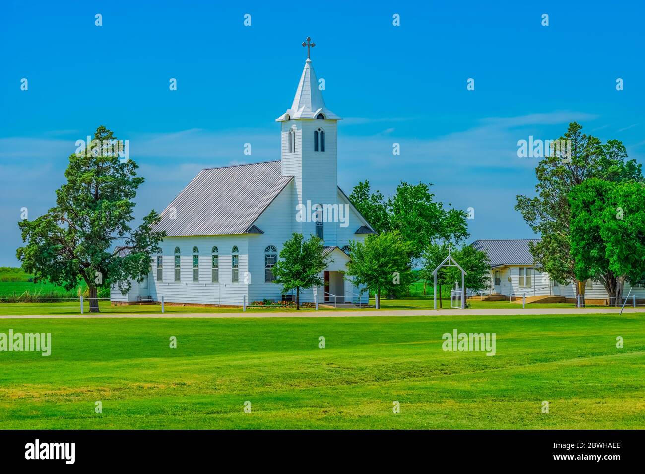 A steepled white church sits in a spring  meadow in Texas. Trees surround the Christian chapel. Stock Photo