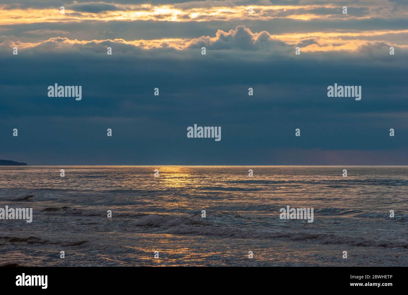 Ocean swell with breaking waves. Sunlight shining through openings in