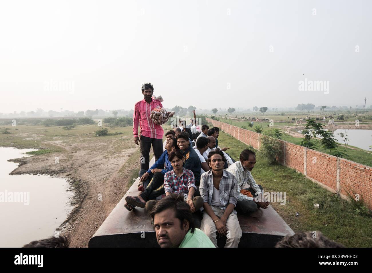 Men on top of overcrowded train passes through a small town in Madhya Pradesh, India. Indian Railways. Stock Photo