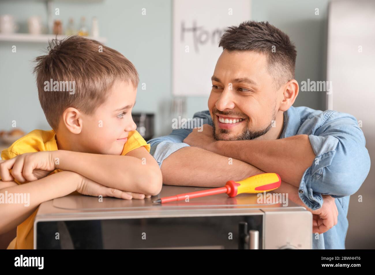 Little son helping his father to repair microwave oven in kitchen Stock ...