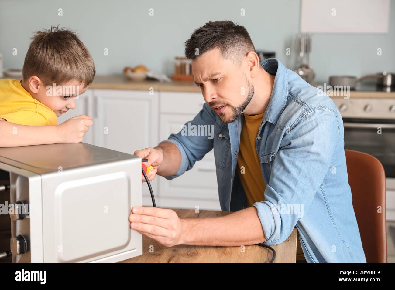Little son helping his father to repair microwave oven in kitchen Stock ...