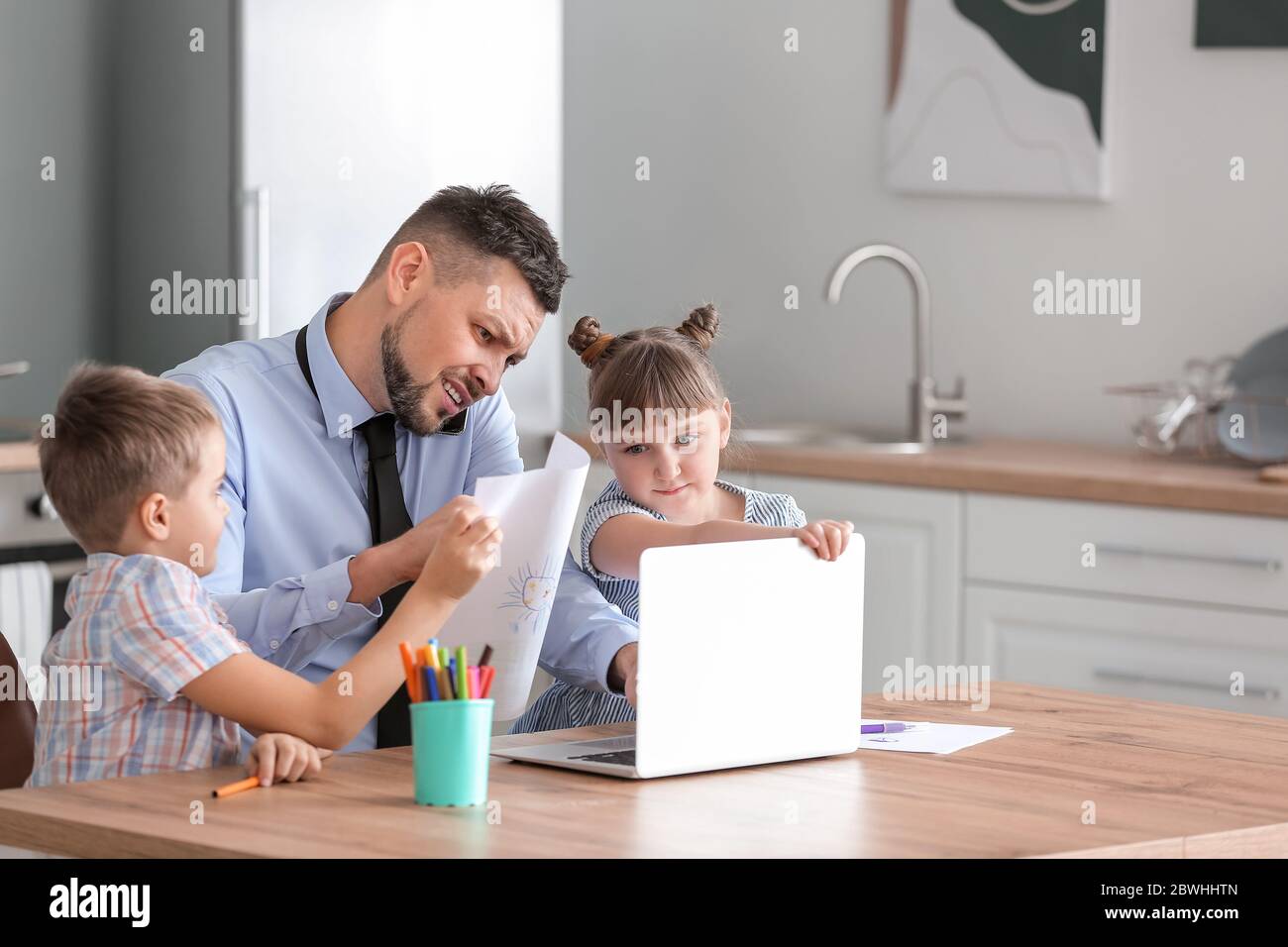 Little children keeping father from his work at home Stock Photo