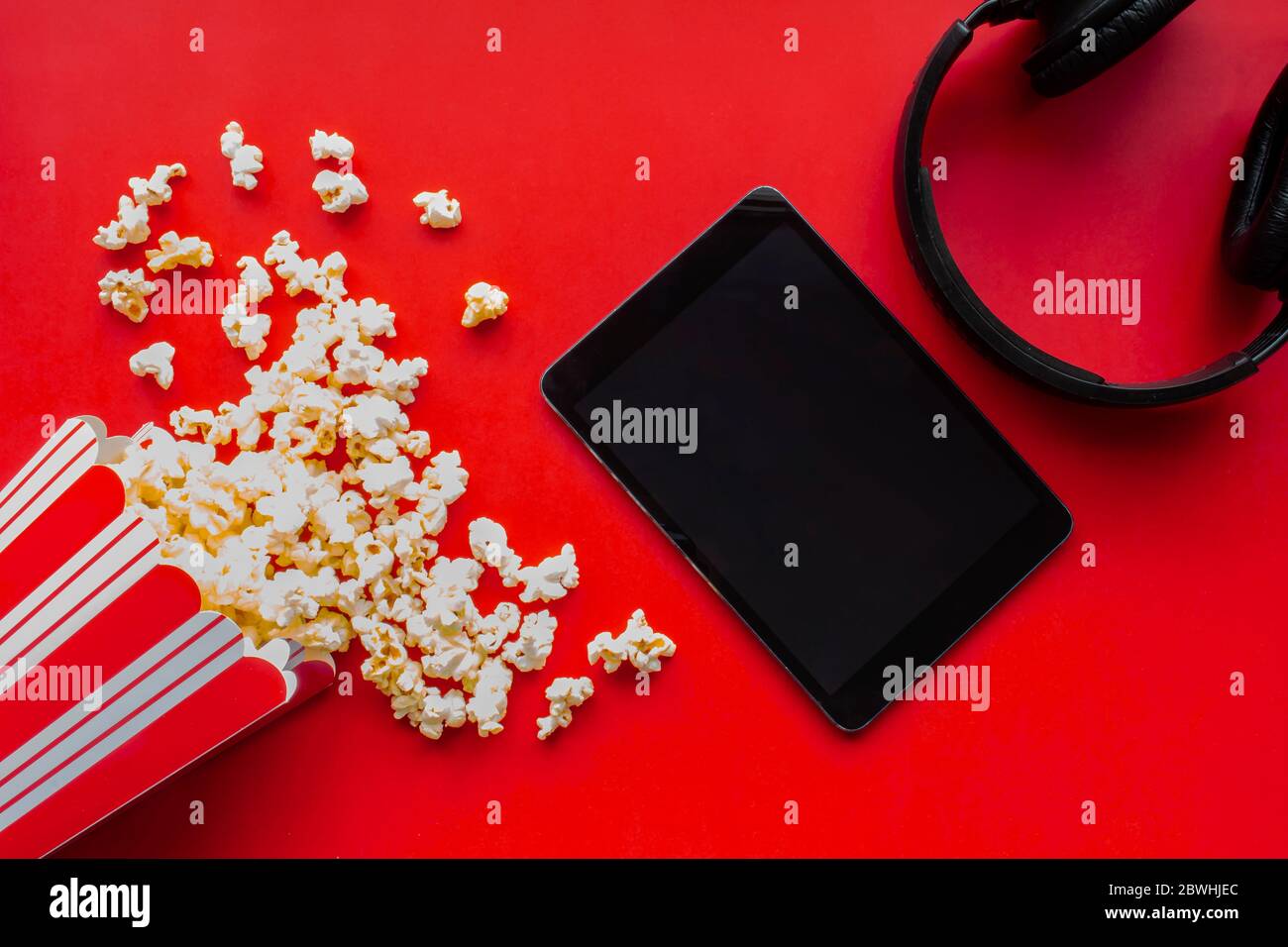 A tablet on a red background with popcorn and headphones Stock Photo