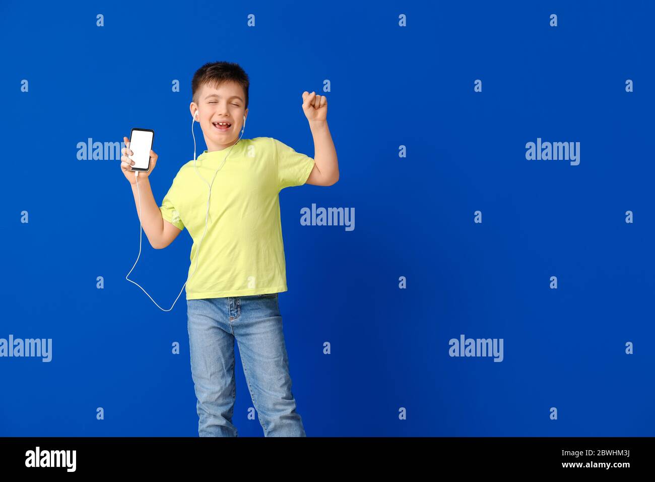 Cute little boy dancing and listening to music against color background