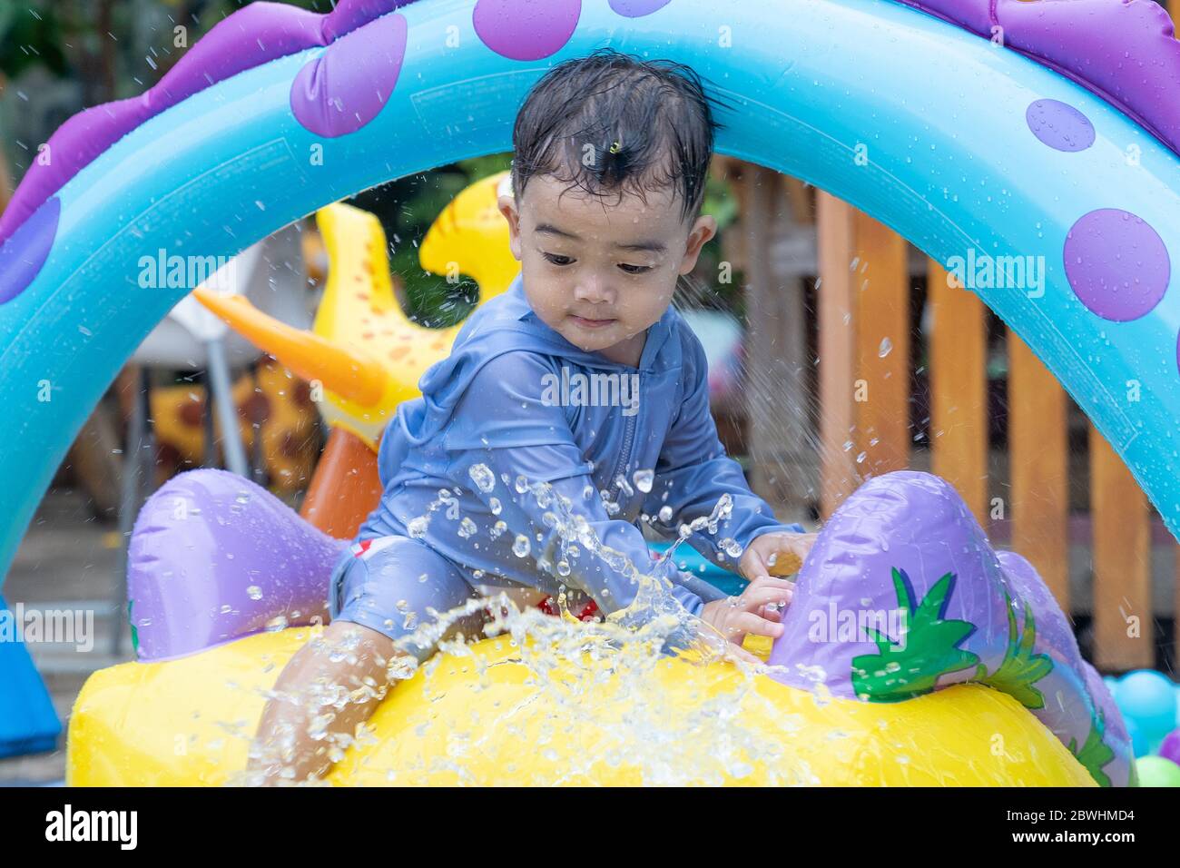 Asian cute baby boy playing in inflatable baby pool. Kids swim and splash in colorful garden play center. Happy little girl playing with water toys on Stock Photo