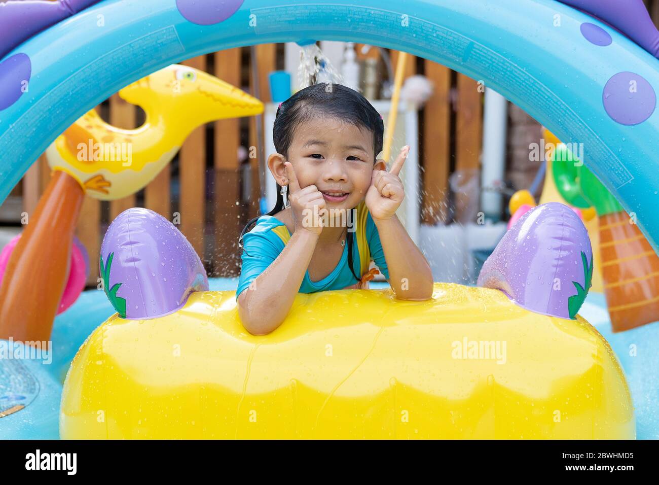 Asian cute girl playing in inflatable baby pool. Kids swim and splash in colorful garden play center. Happy little girl playing with water toys on hot Stock Photo