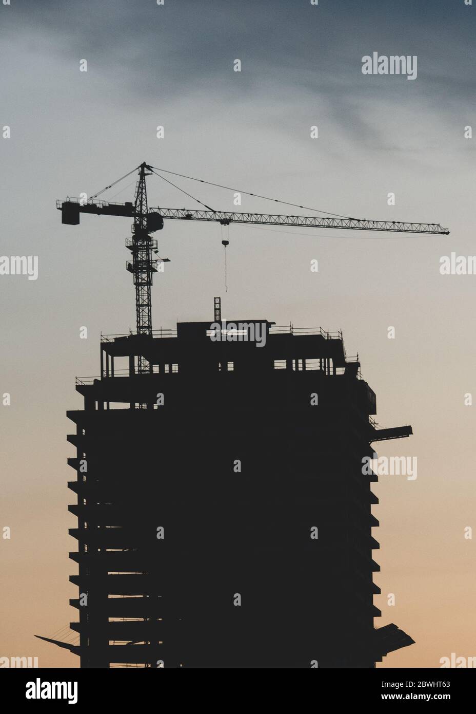 Silhouette of tower crane constructing high building in city. Stock Photo