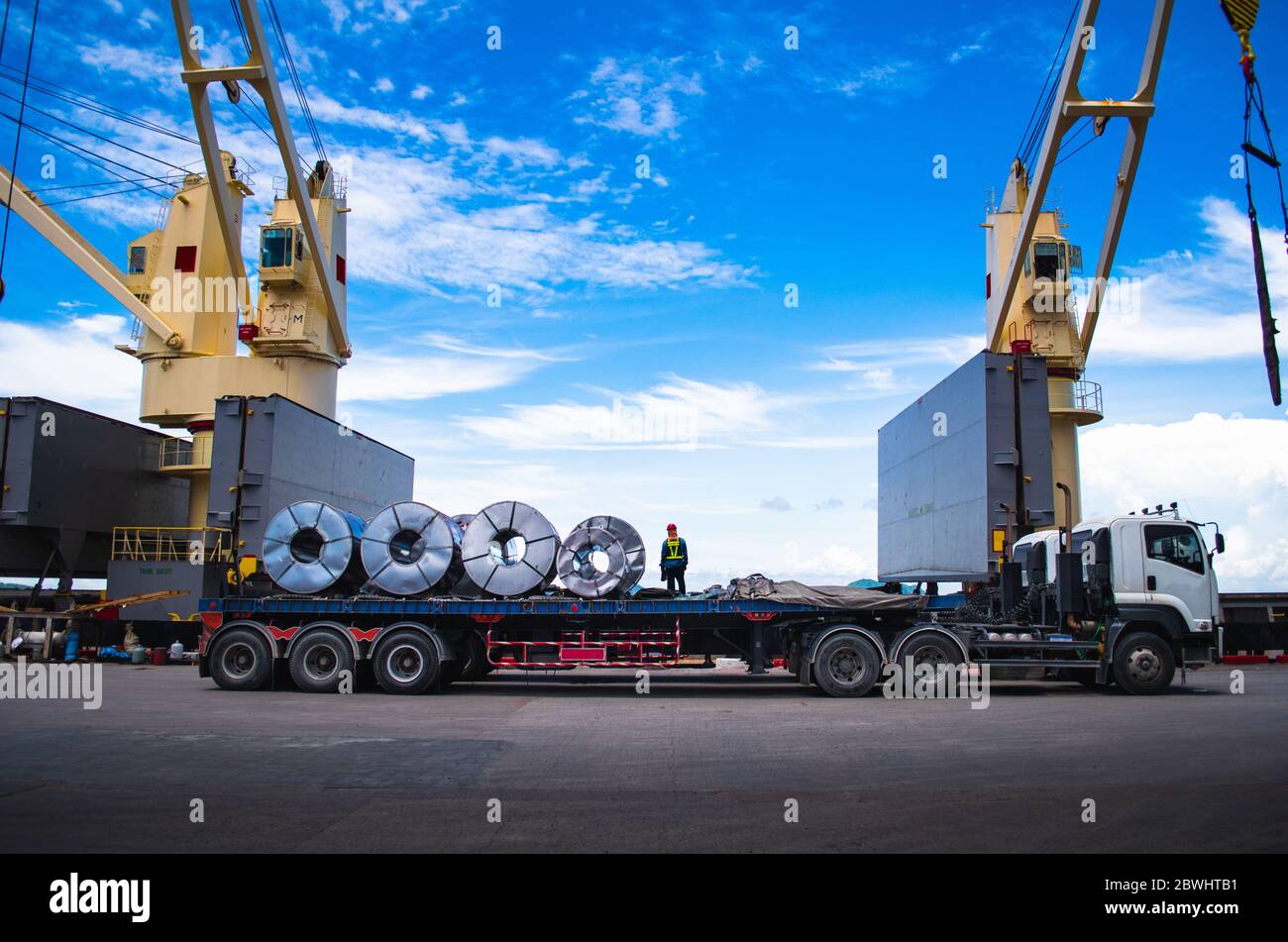 Truck receive steel coils alongside large cargo ship at port Stock Photo