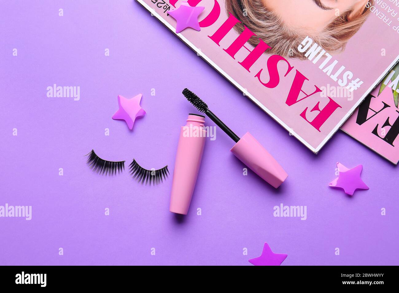 Mascara with fake eyelashes and fashion magazines on color background Stock Photo