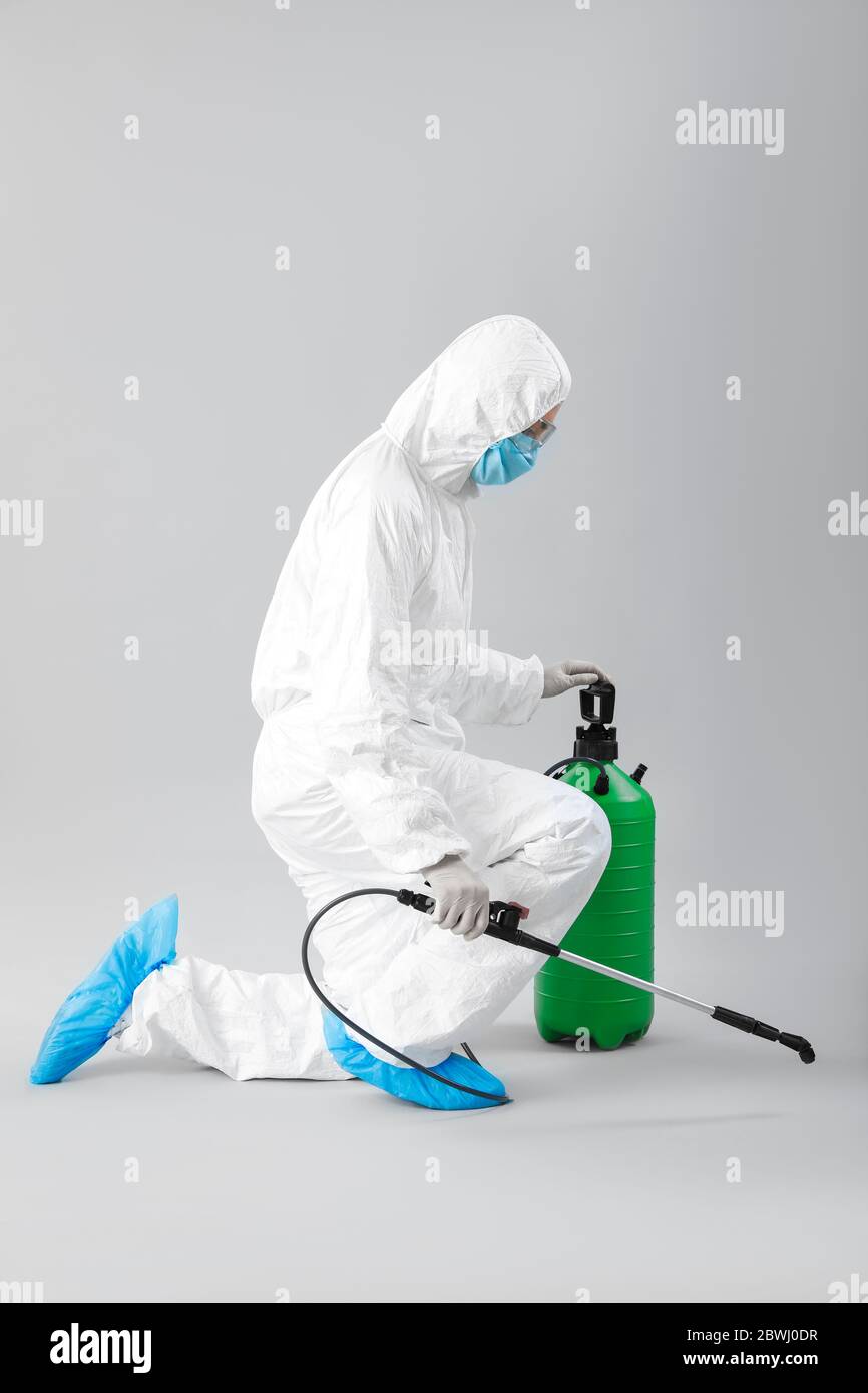 Worker in biohazard suit and with disinfectant on grey background Stock Photo