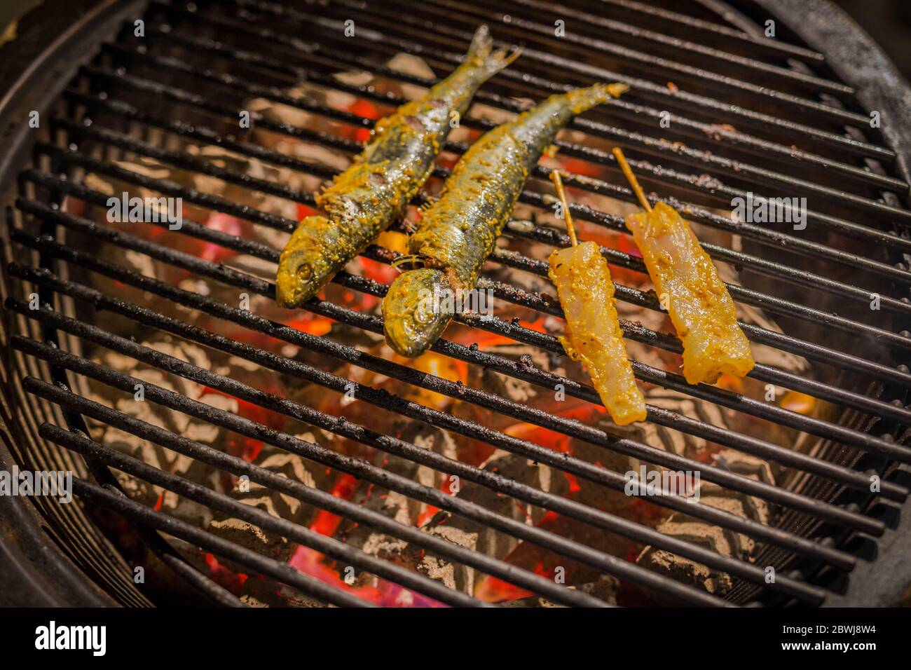Fish grilling on a barbecue with lemon slices and rosemary with fish skewer on hot coal, outdoors barbecue Stock Photo