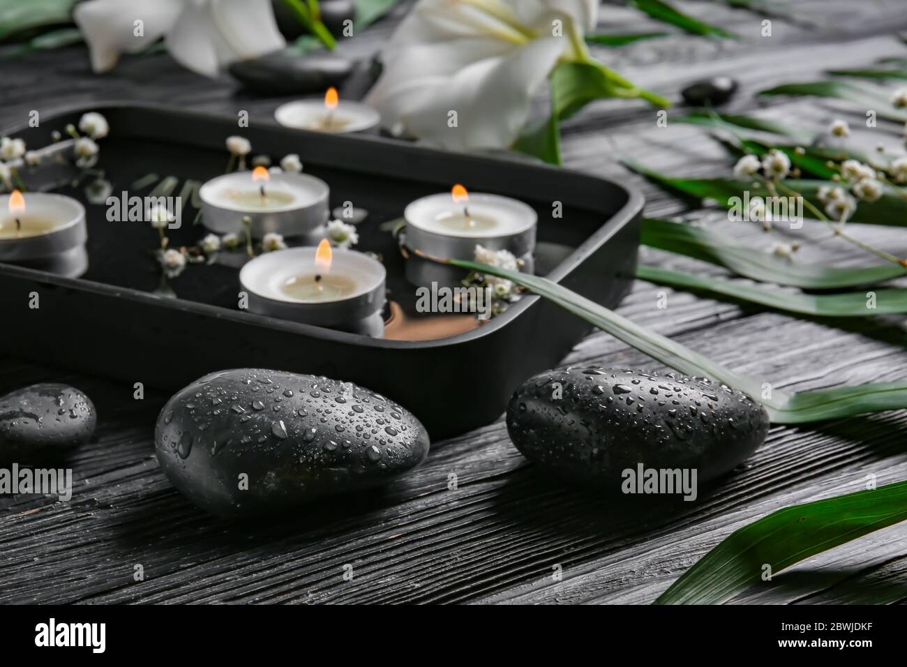 Spa stones and plate with water and candles on dark wooden background ...