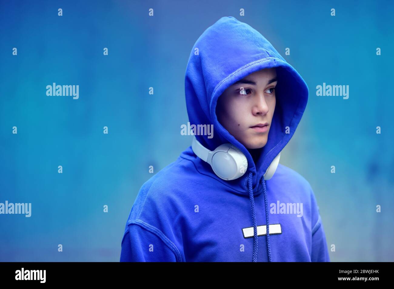 Young man wearing a hoodie with earphones around his neck looking off to the side with a serious thoughtful expression Stock Photo