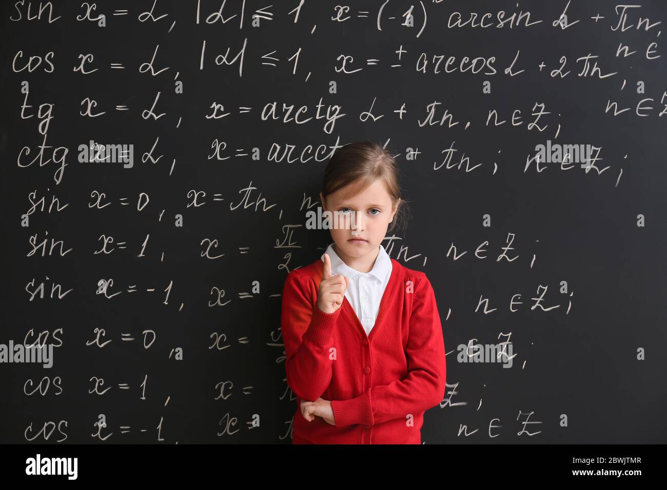 Cute little schoolgirl with raised index finger near blackboard in classroom Stock Photo