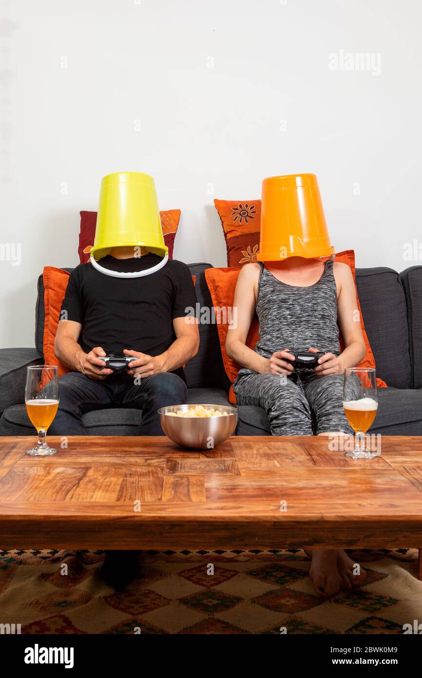 Young couple play video games sitting comfortably on the sofa at home. They drink beer and eat chips Stock Photo