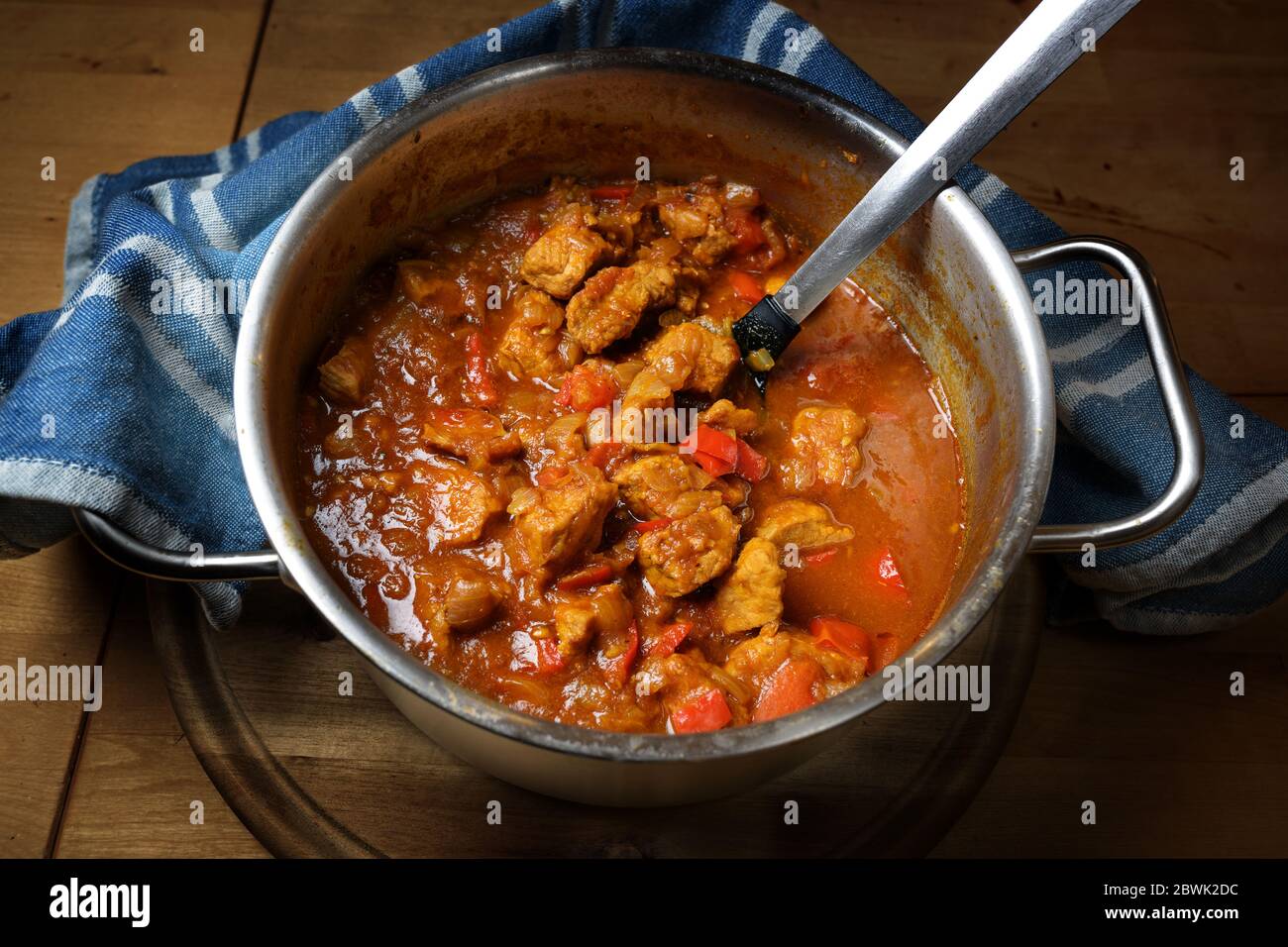 Freshly cooked goulash or stew from pork meat with red peppers and onions in a stainless steel pot on a rustic wooden board, selected focus Stock Photo