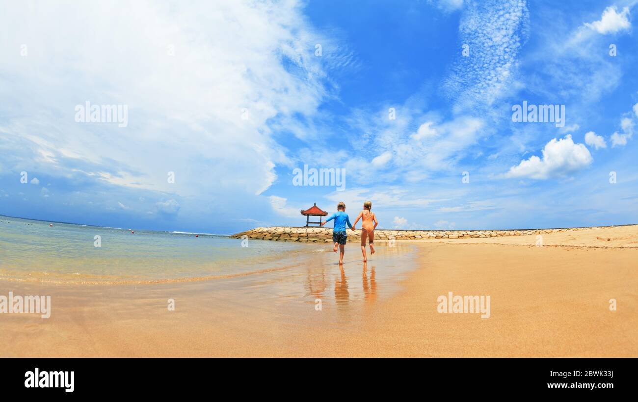 Happy family have fun on tropical sea beach resort. Funny siblings run with splashes by water pool along surf edge. Kids lifestyle, people swimming Stock Photo