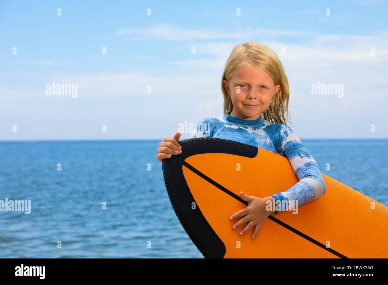 Happy baby girl - young surfer learn to ride on surfboard with fun on sea waves. Active family lifestyle, kids outdoor water sport lessons, Stock Photo