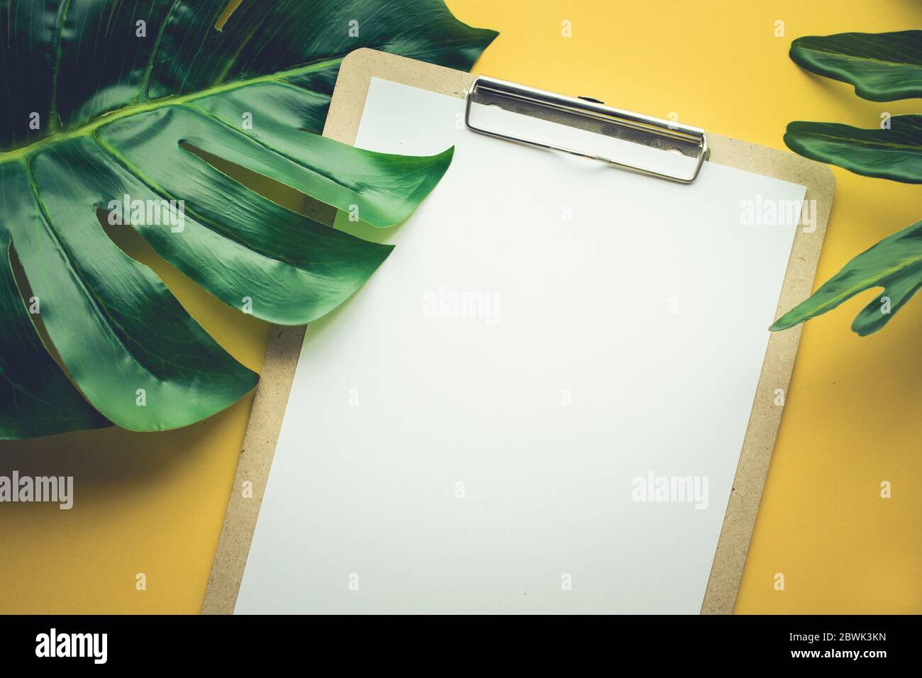 Blank white notepaper with tropical leaves laying on yellow table.Home office,workspace design backgrounds,flat lay,top view Stock Photo