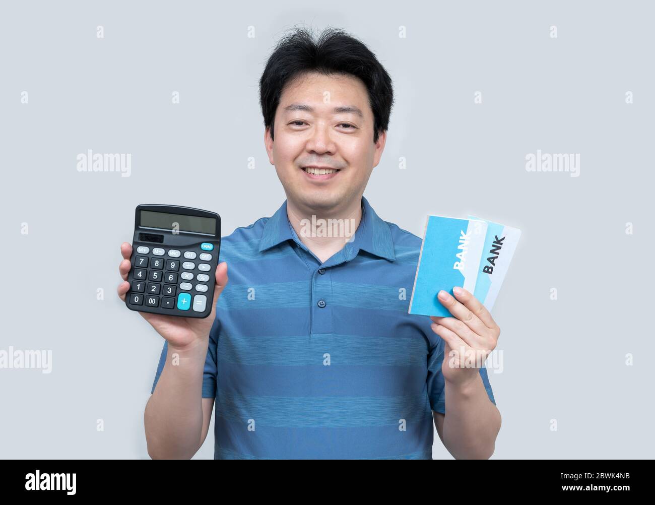 A middle-aged Asian man holding a bank passbook and calculator in his hand on a gray background. Stock Photo