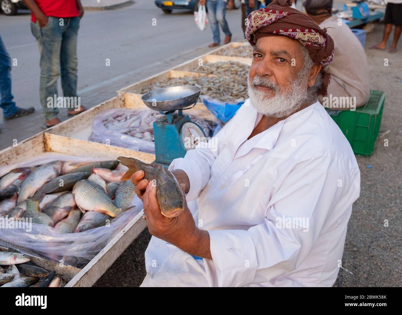 Elderly Omani fishmonger showing a fish at roadside fish market in Muscat, Sultanate of Oman. Stock Photo