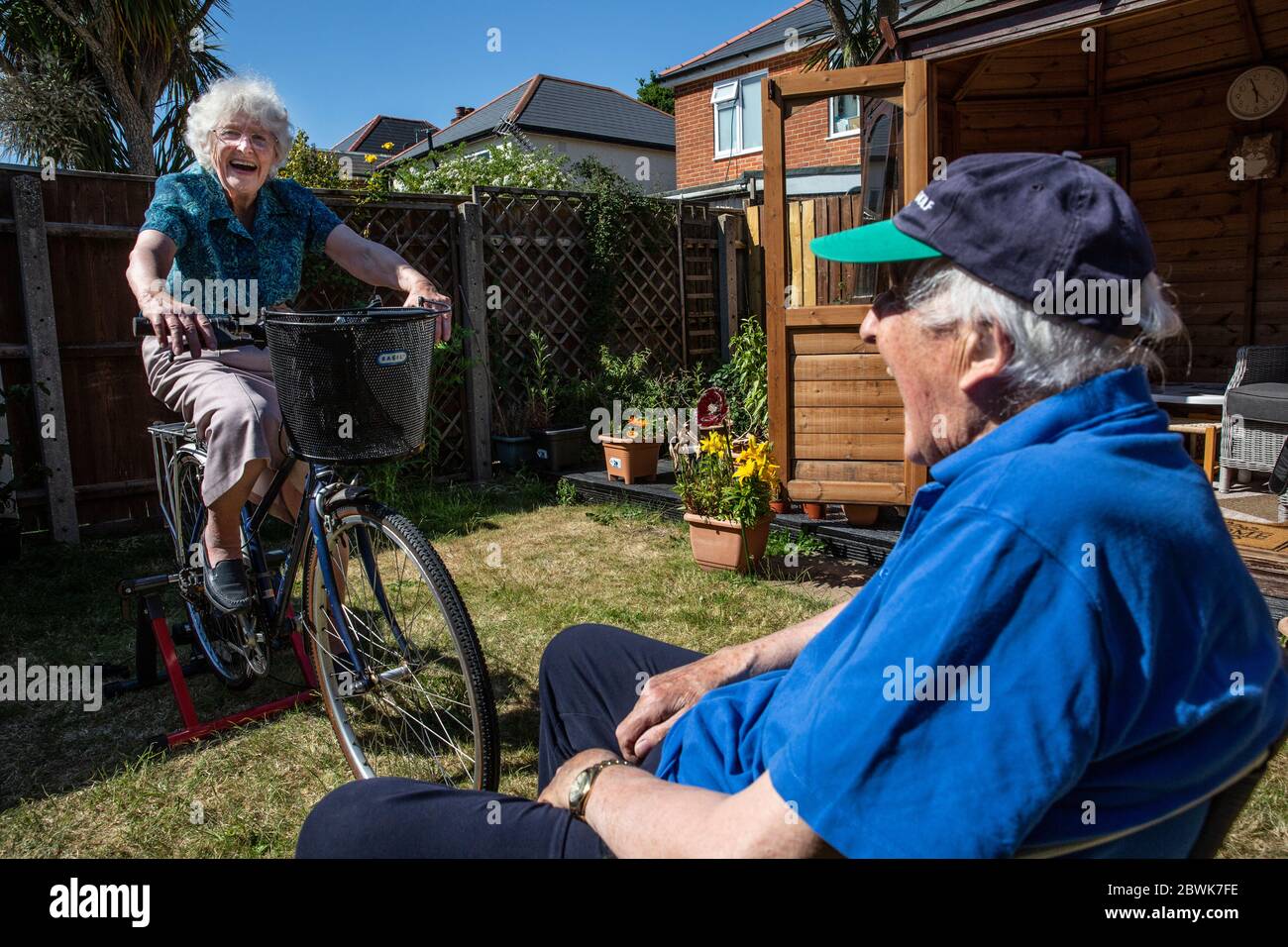 Elderly couple both in their 80's keeping fit on a bicycle trainer stand in their back garden during the coronavirus lockdown, Southwest England, UK Stock Photo