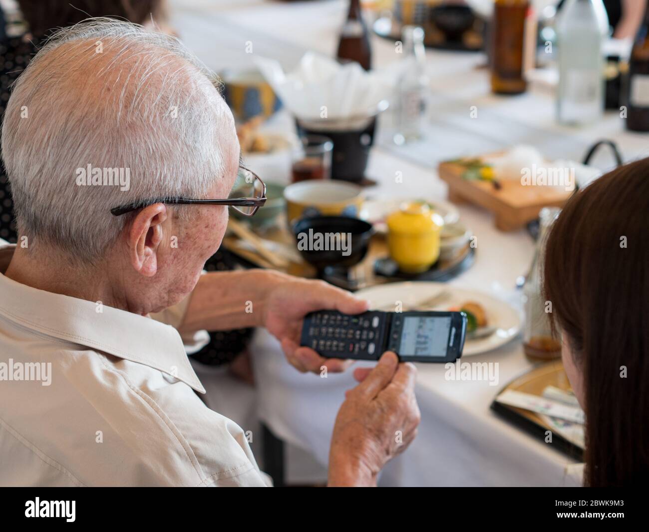 An elderly Asian man struggling to use an old fashioned flip phone Stock Photo