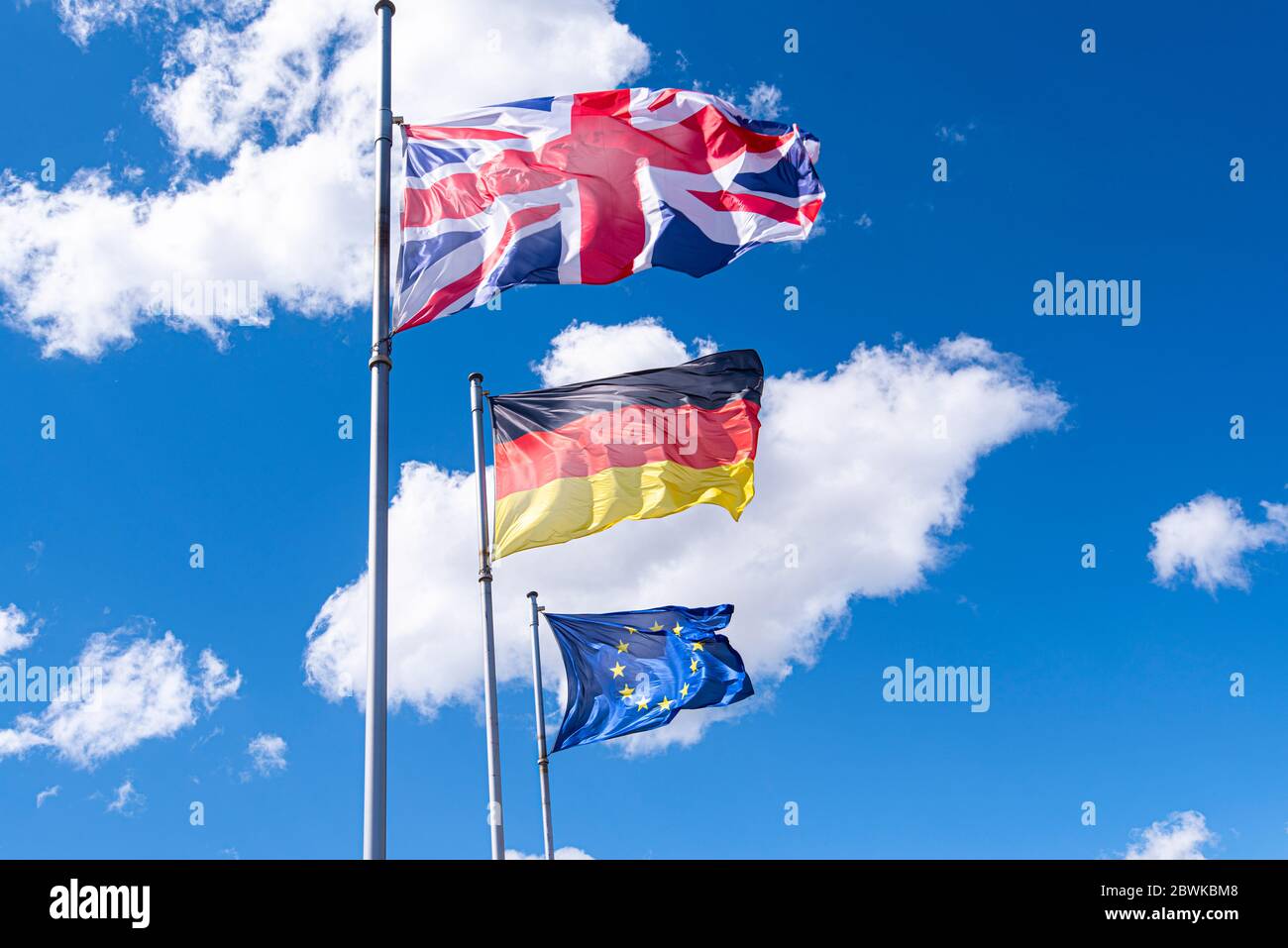 Flags of Germany, Great Britain and European Union in a street. EU, UK and German flags against blue sky Stock Photo