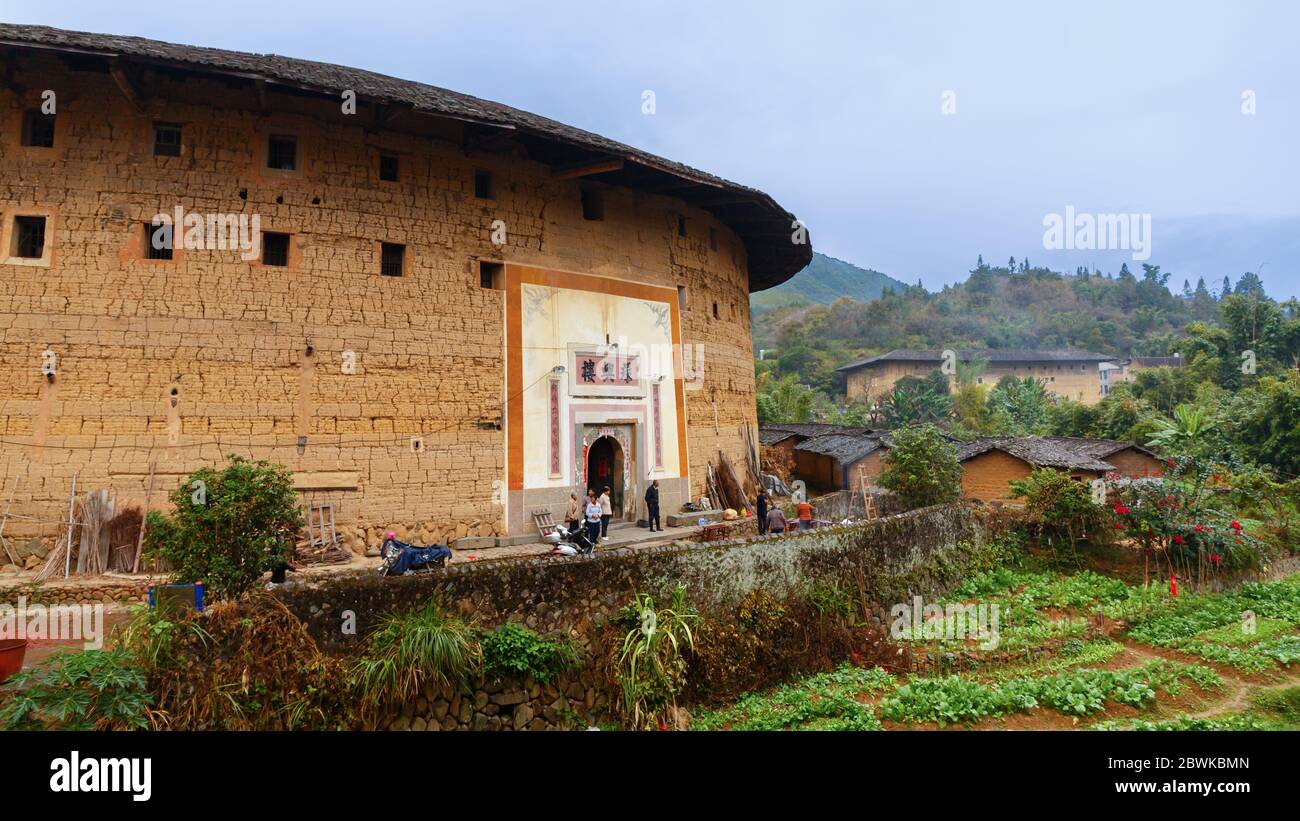 Panorama with a traditional Fujian Tulou within lush green landscape. Stock Photo