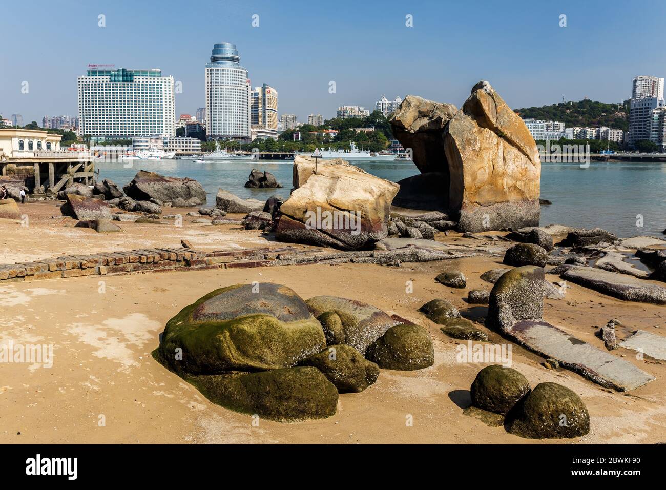Big rocks on the sandy shore of Gulangyu Island. In the background anchoring ships and a view on the Xiamen skyline. Stock Photo