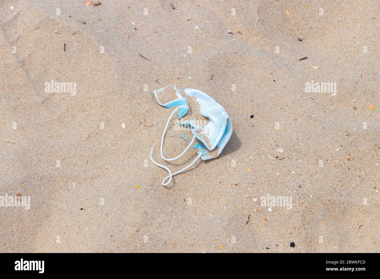 A discarded surgical protective mask on the sand beach. Dirty used medical mask discarded on the beach after be used during the coronavirus covid-19 e Stock Photo