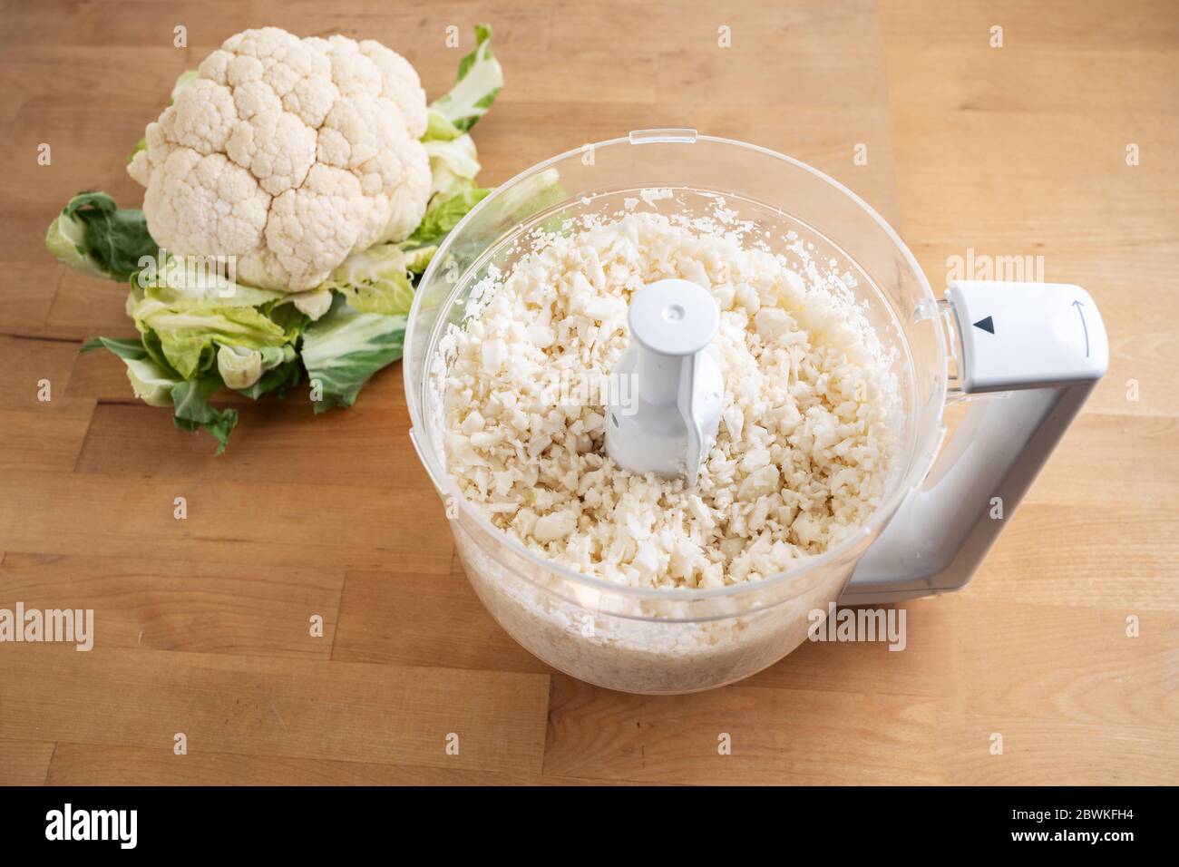 cauliflower shredded in a food processor for healthy low carb pizza crust or as vegetable rice replacement on a wooden kitchen table Stock Photo
