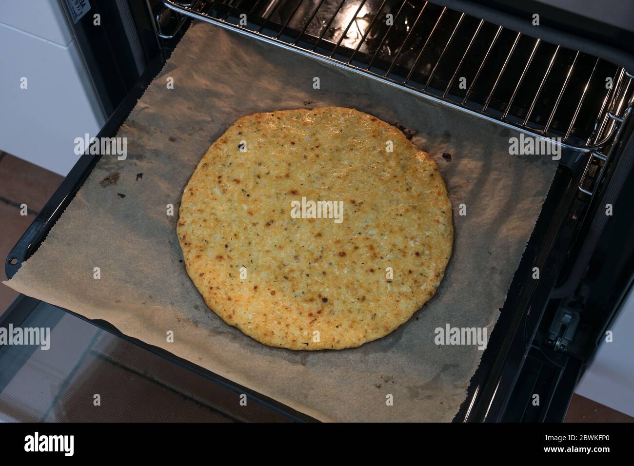 Baked pizza crust from shredded cauliflower and cheese on a baking tray in the oven, healthy slimming alternative for low carb and ketogenic diet, sel Stock Photo