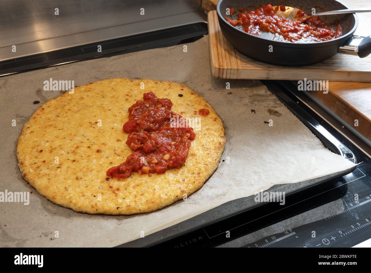 Baked pizza base from shredded cauliflower and cheese half covered with tomato sauce, cooking a healthy alternative for slimming with low carb or keto Stock Photo