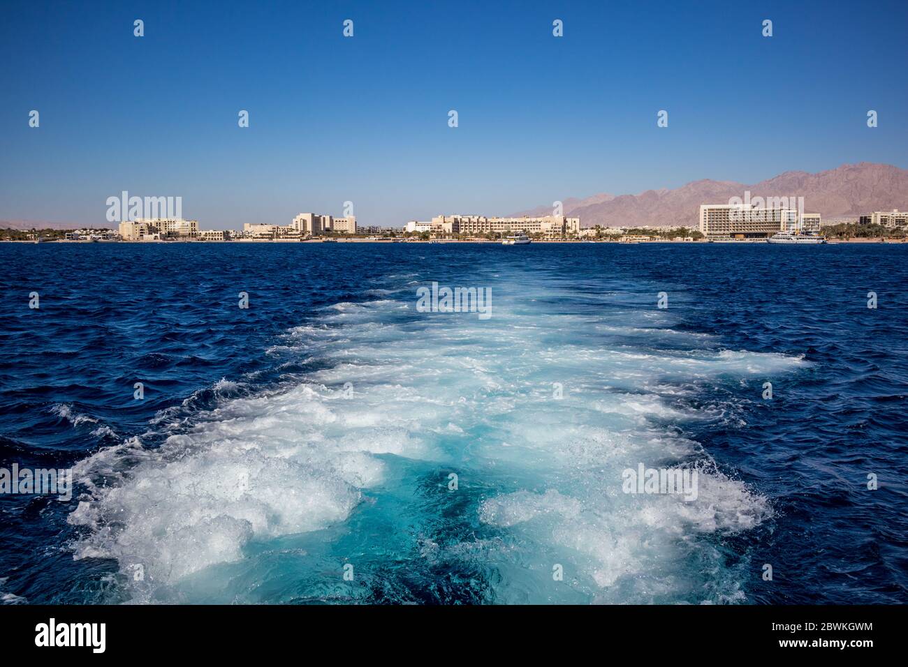 Gulf of Aqaba as seen from tourist boats, Jordan. Some front line hotels and the crystal blue water of Red Sea, sunny winter afternoon, water foam from the speeding vessel Stock Photo