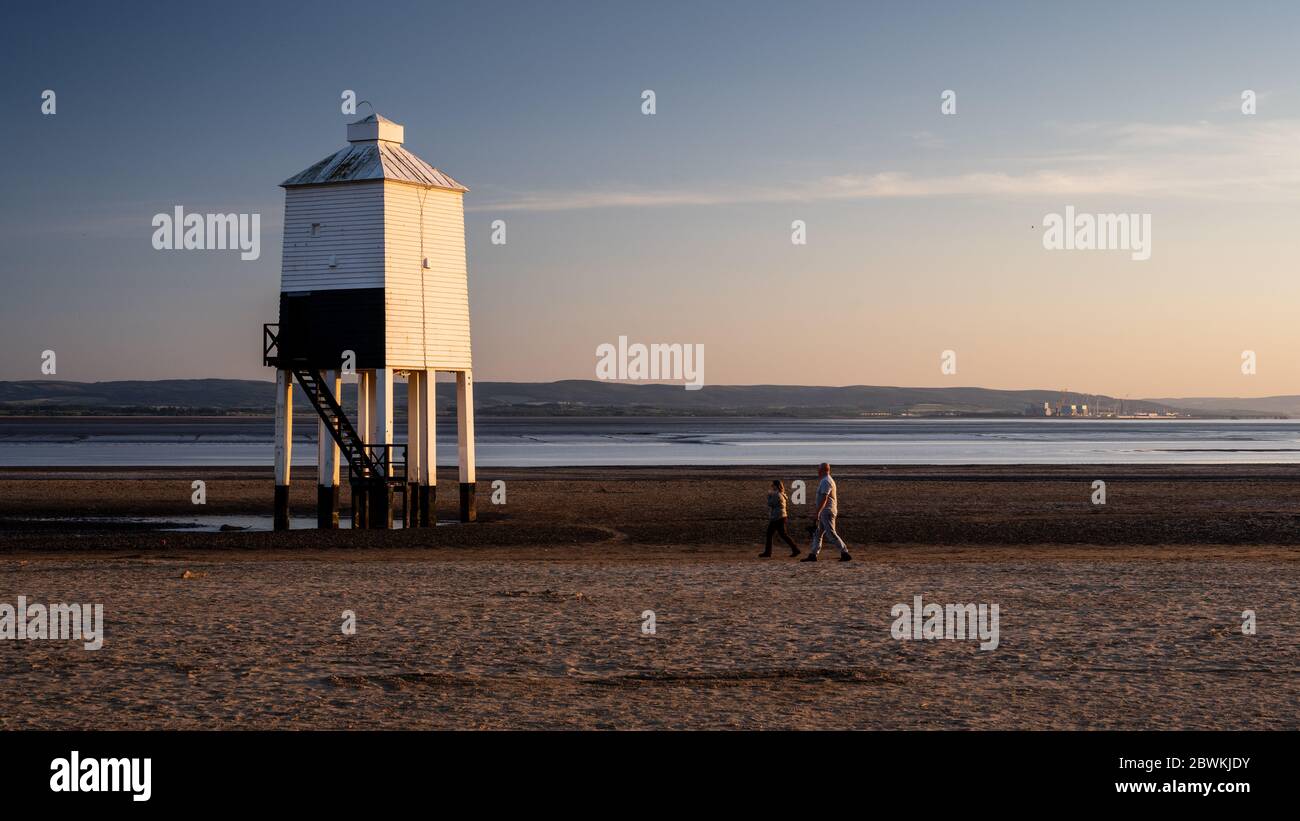 Burnham-on-Sea, England, UK - May 31, 2020: A couple walk past the Low Level Lighthouse on Burnham Beach on the Bristol Channel, with Hinkley Point Po Stock Photo