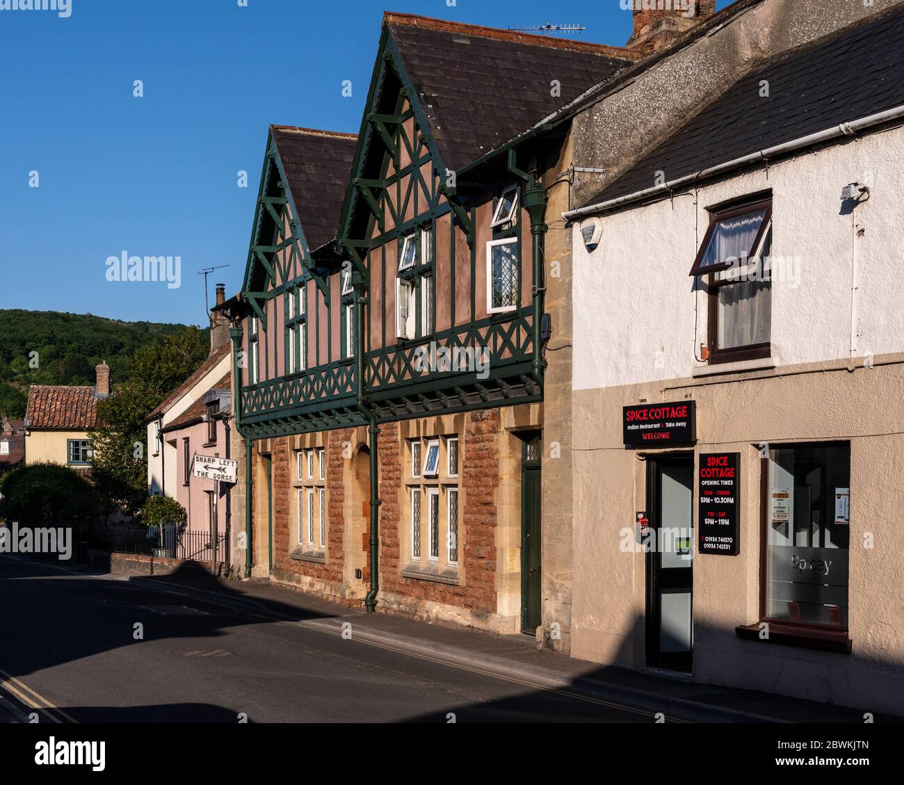 Cheddar, England, UK - May 31, 2020: Sun shines on houses in the town of Cheddar, beside an old-fashioned sign giving directions to Cheddar Gorge. Stock Photo