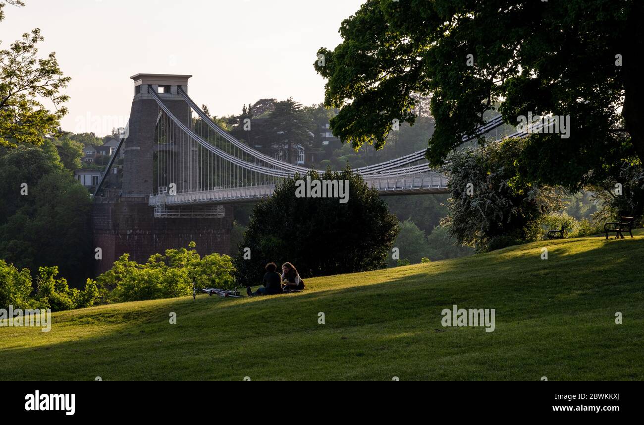 A couple sit on grass in Clifton Down park beside the Clifton Suspension Bridge in Bristol. Stock Photo