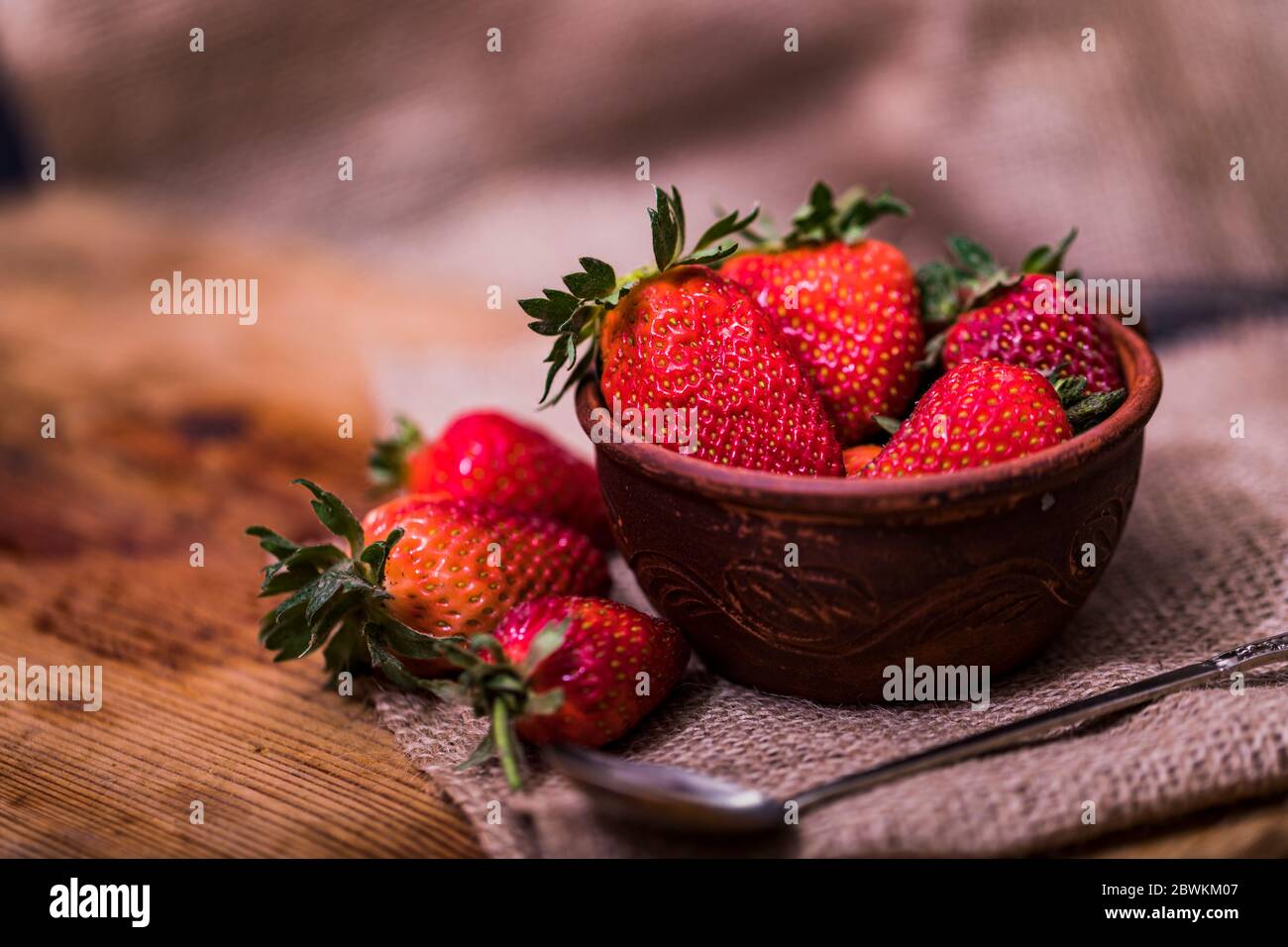 Fresh strawberries in a bowl on wooden table with low key scene. Stock Photo
