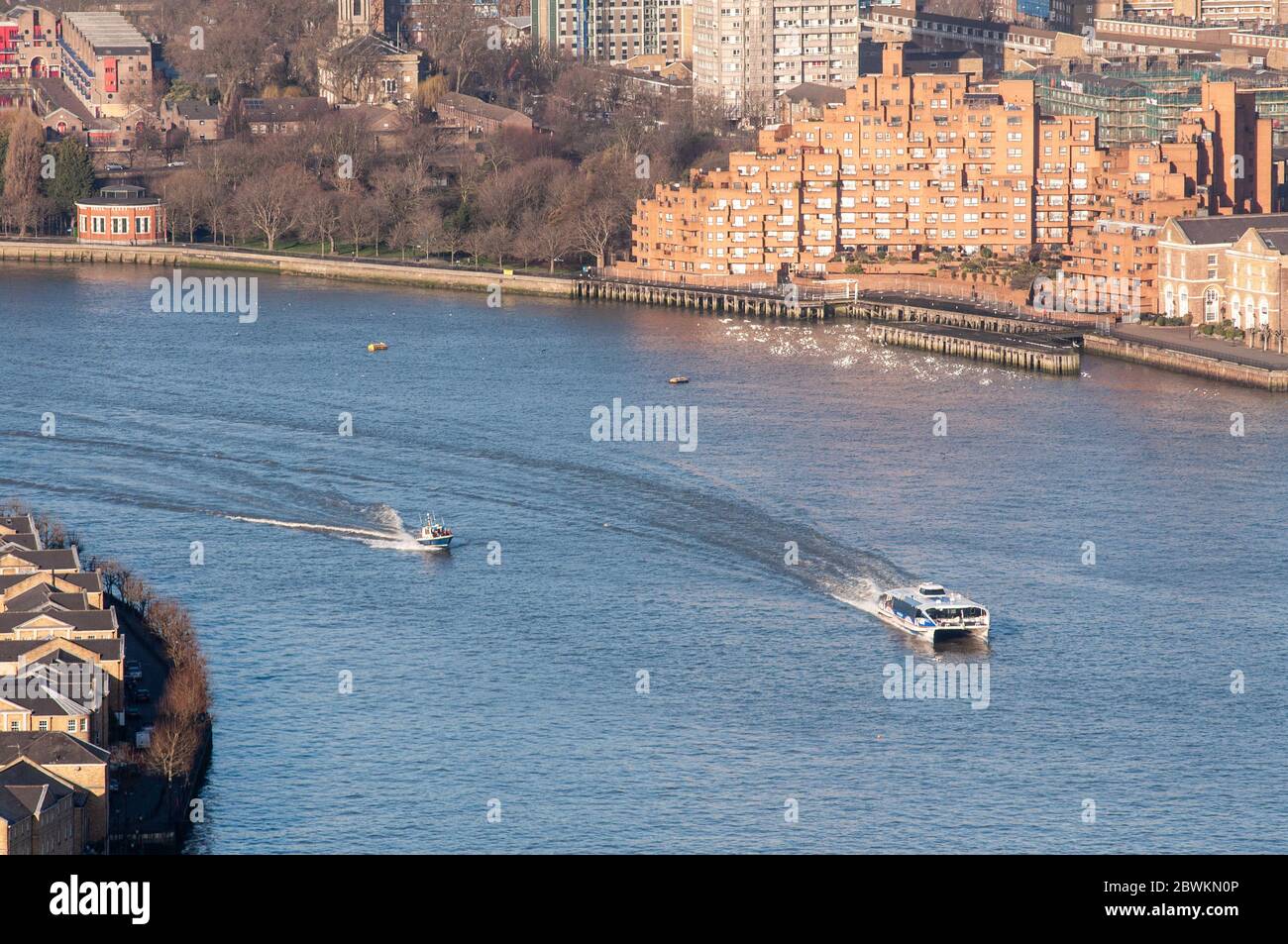 London, England, UK - February 27, 2015: A Thames Clipper ferry and speed boat travel along the River Thames past Wapping and Rotherhithe in East Lond Stock Photo