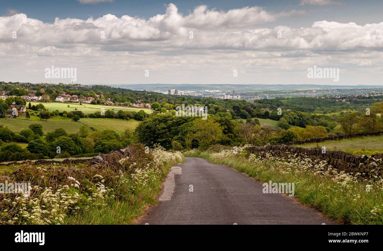 A country lane descends from the Peak District hills into the Mayfield Valley and the suburbs of Sheffield, with the city centre cityscape in the dist Stock Photo