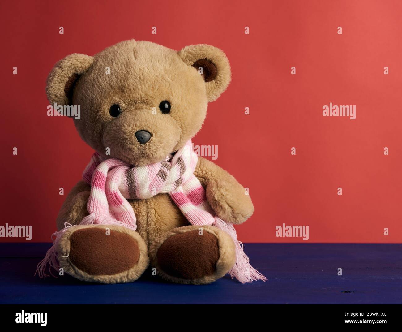 cute brown teddy bear in a colored knitted scarf sitting on a red ...