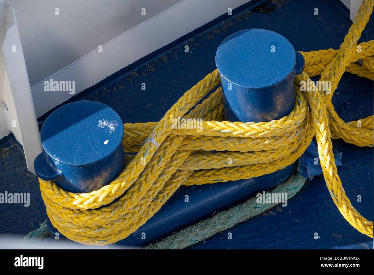 yellow ship rope tied around blue mooring bollards on a metal boat