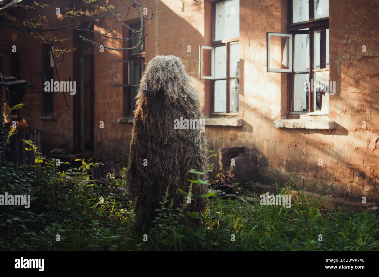 Special camouflage ghillie suit for military, snipers and intelligence agents. Against the background of the destroyed house. Stock Photo