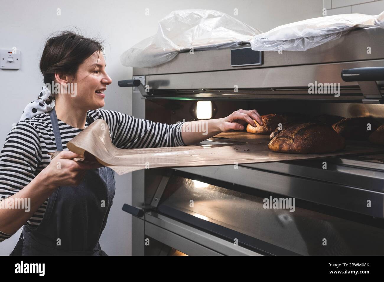 Artisan bakery making special sourdough bread, baker removing a tray of baked loaves from the oven. Stock Photo