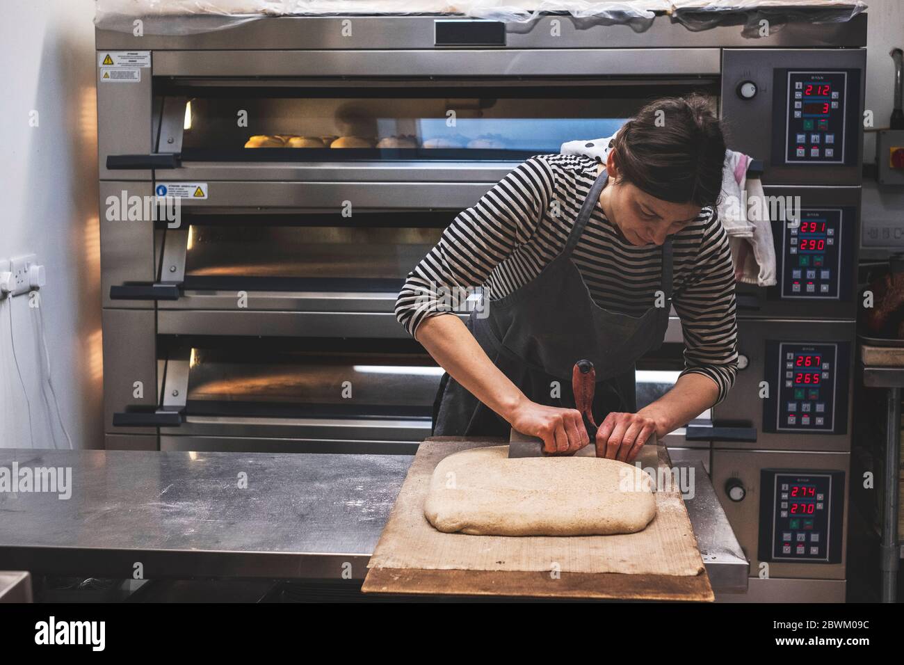 Baker dividing dough in sections for baking by a large commercial oven. Stock Photo