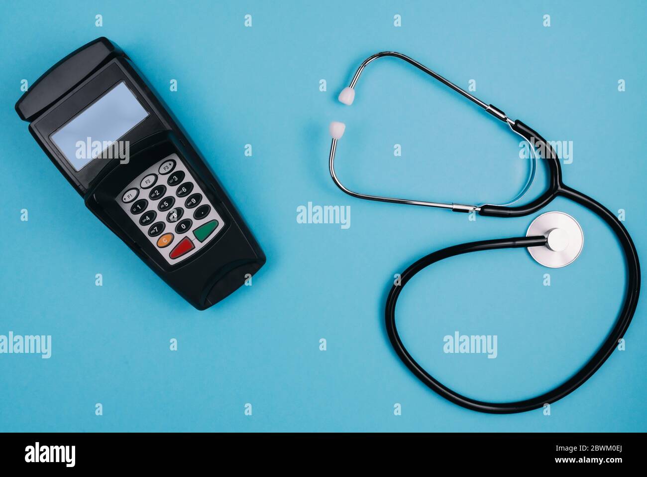 cost and payment for medical treatment or copay concept, above shot of stethoscope and credit card reader on blue desk background Stock Photo