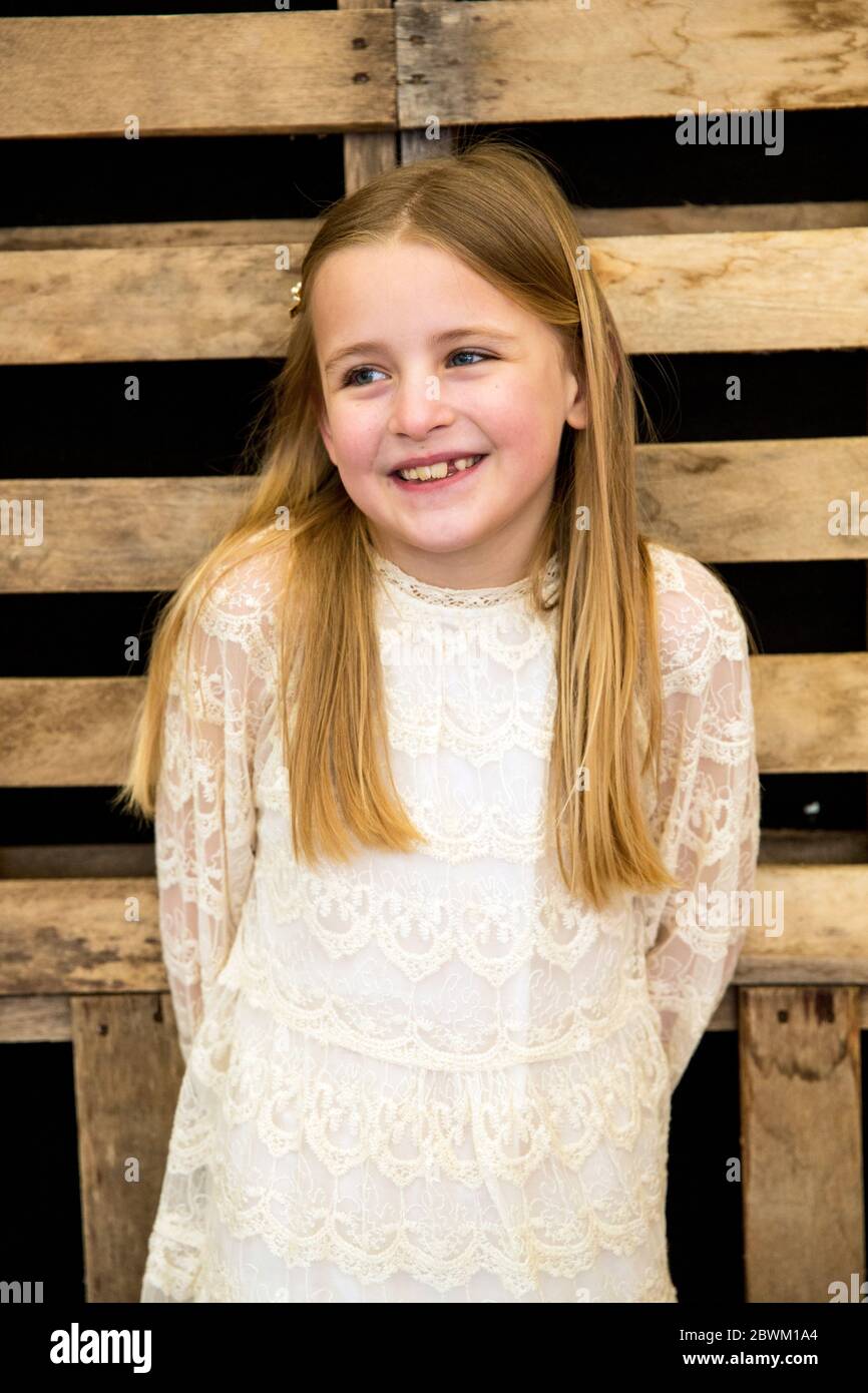 Portrait of smiling girl wearing cream coloured lace dress during naming ceremony in an historic barn. Stock Photo