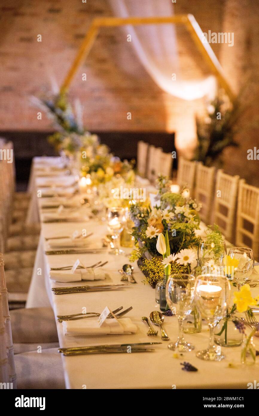 Long dining table with festive place settings for a naming ceremony in an historic barn. Stock Photo